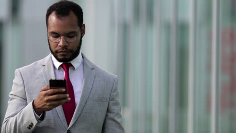 Front-view-of-focused-businessman-using-smartphone-during-stroll